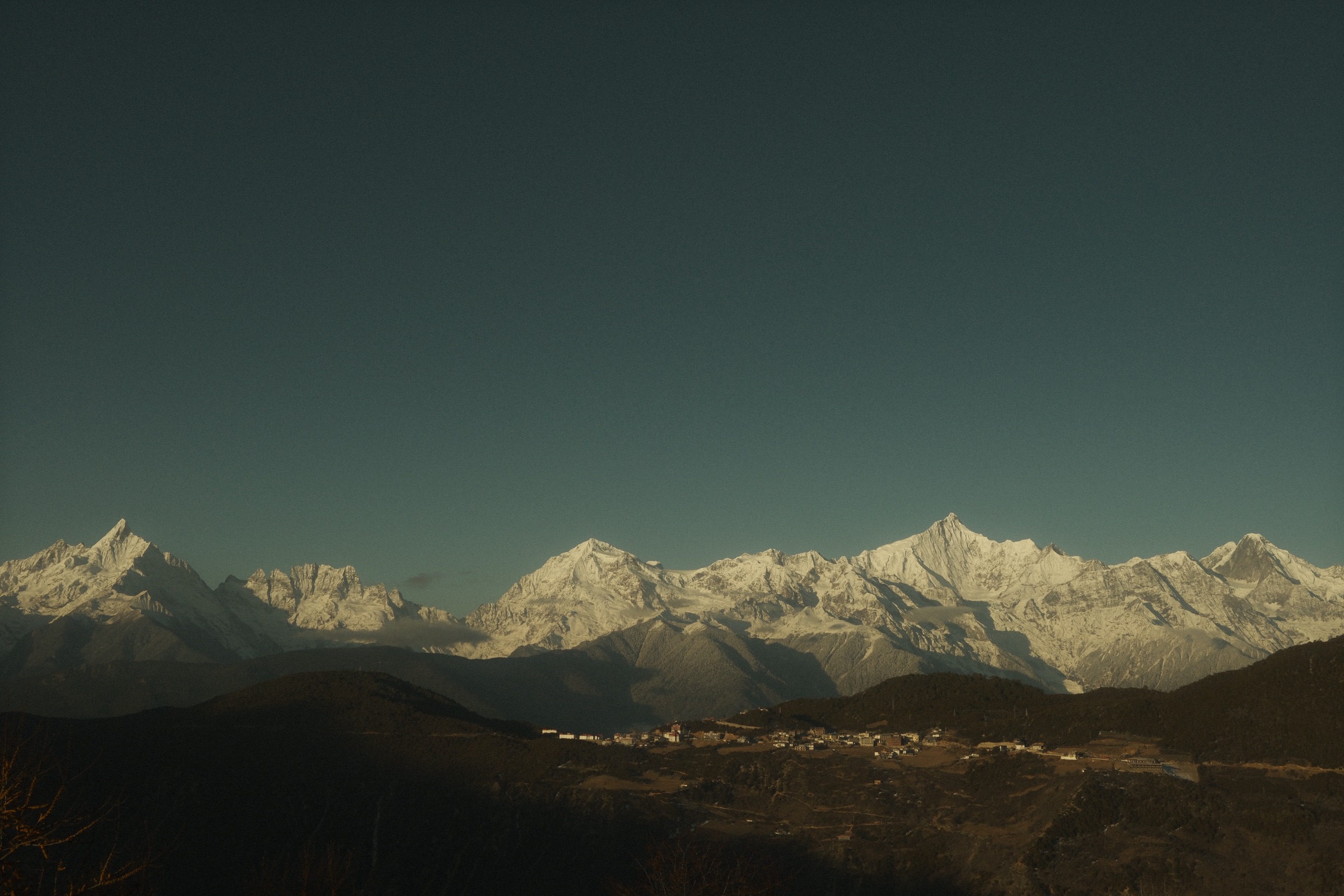 Meili Snow Mountain range under clear blue sky with village below