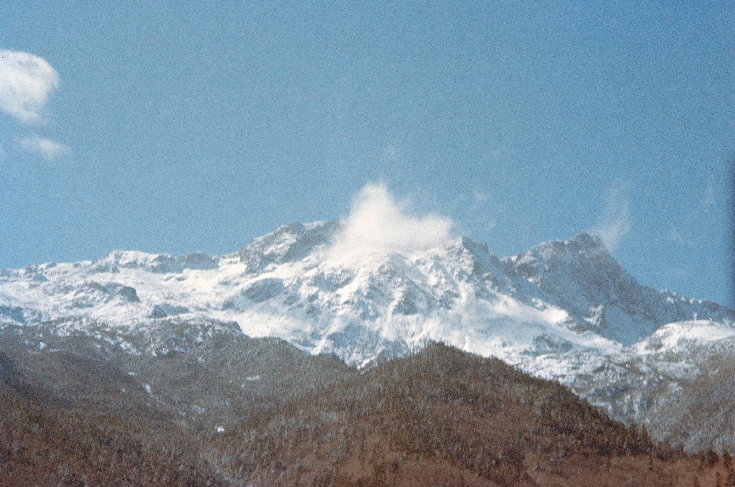 Snow-capped mountain with clouds drifting under bright blue sky