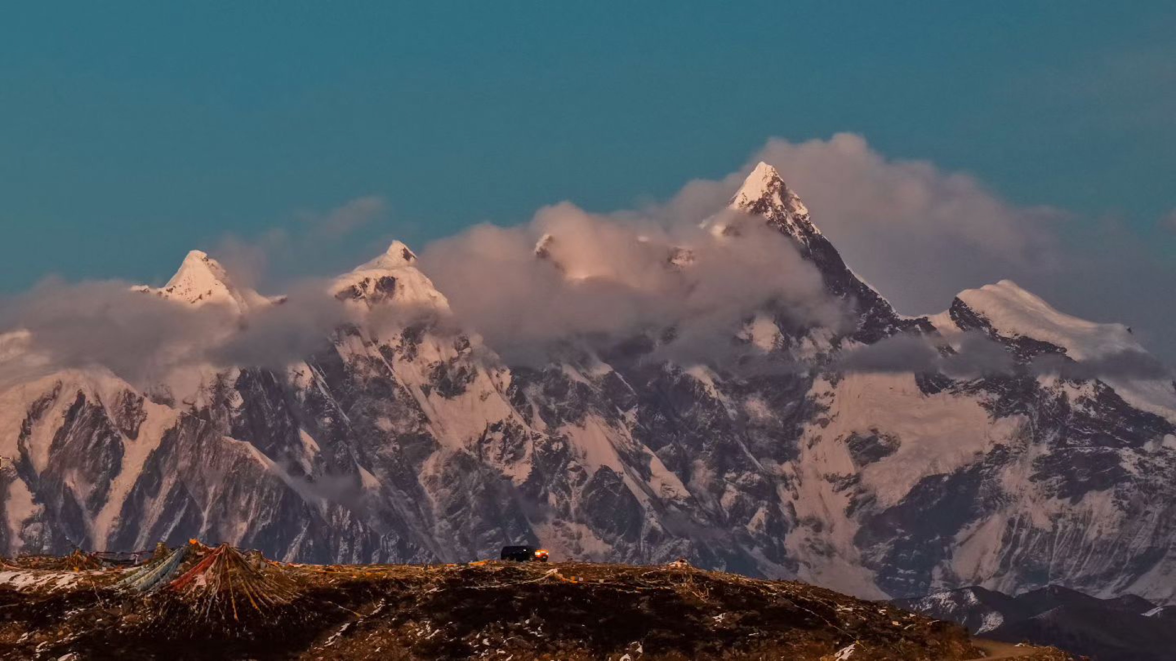 Dramatic snow peaks with prayer flags in the foreground at dusk